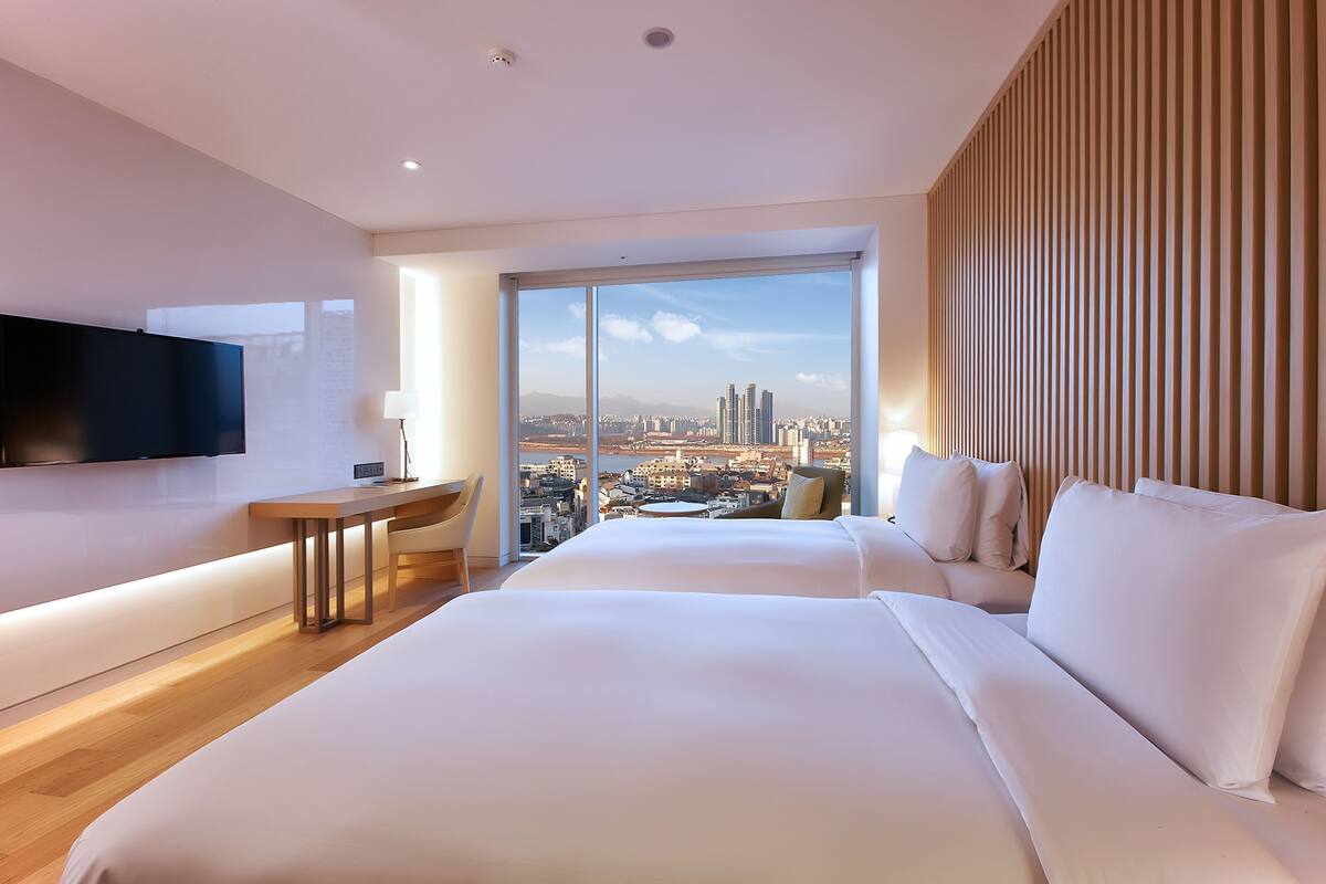 Una habitación de hotel moderna con una cama grande, un escritorio y un televisor. La habitación tiene un ventanal con vistas a la ciudad.