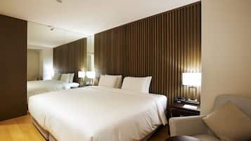 A modern hotel room with a large bed, a sofa, a desk with a lamp, and a large mirror.