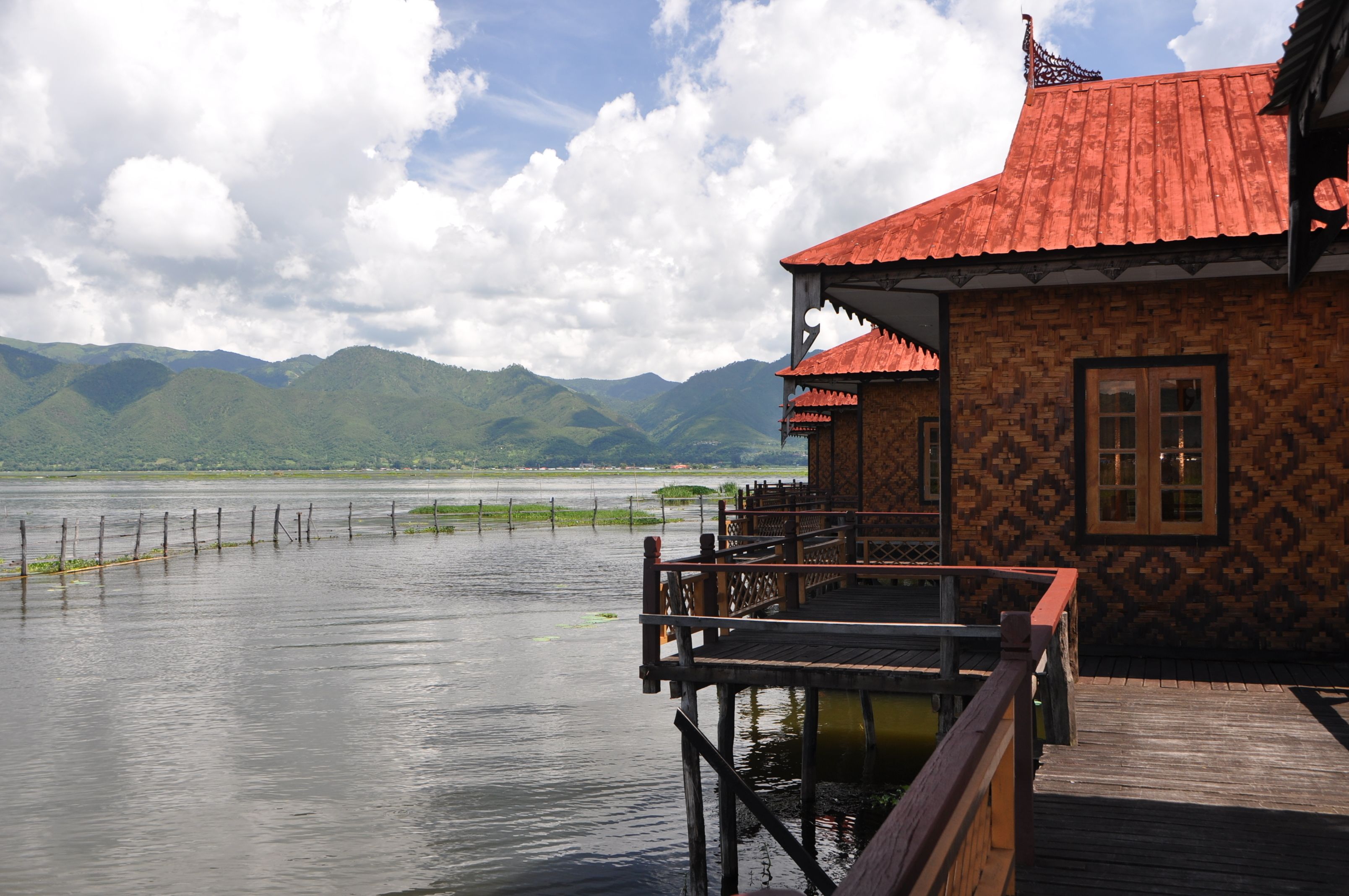 A wooden structure with a red roof overlooking a calm lake and mountains.