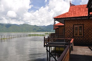 Une construction en bois, surmontée d’un toit rouge, qui surplombe un lac paisible et des montagnes.