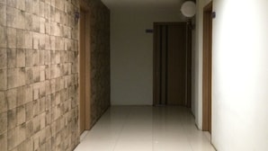 A hallway with tiled flooring, a brick wall on one side, and a plain wall on the other. There is a door at the end of the hallway.