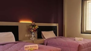A hotel room with two beds, each with a 'Pax Hotel' sign, a vase with flowers, and a window with blinds.