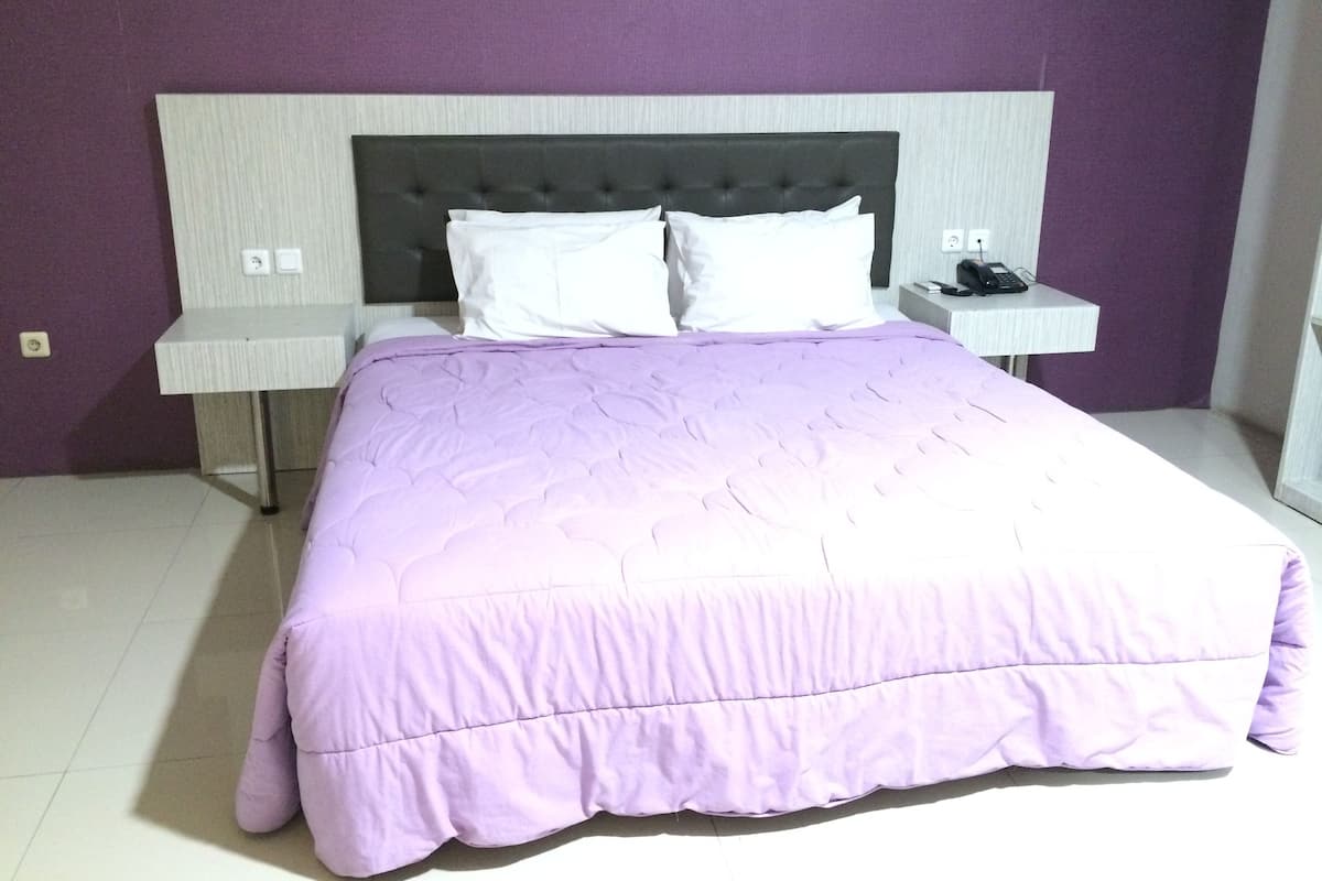 A neatly made bed with a purple bedspread and white pillows, flanked by two bedside tables with lamps, in a room with purple walls.