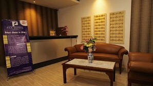 A hotel lobby with a brown leather sofa, a wooden coffee table with a vase of flowers, and a reception desk.