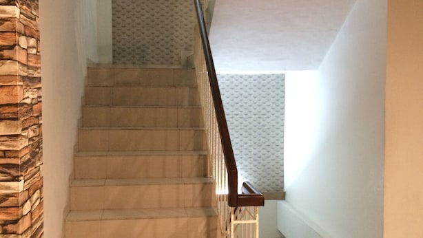 A staircase with a wooden handrail and a stone wall on one side.