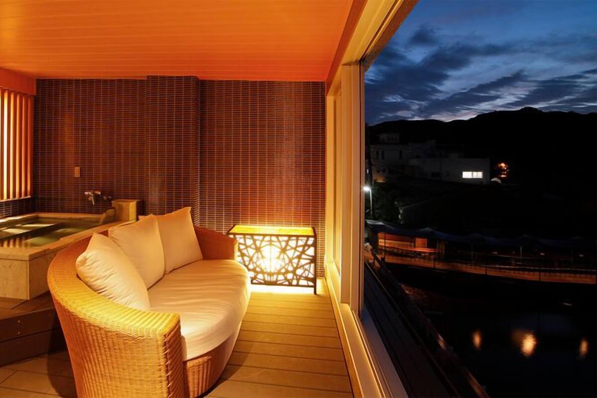 Un interior moderno con piso de madera, un sofá, un jacuzzi y vista a un cuerpo de agua al atardecer.