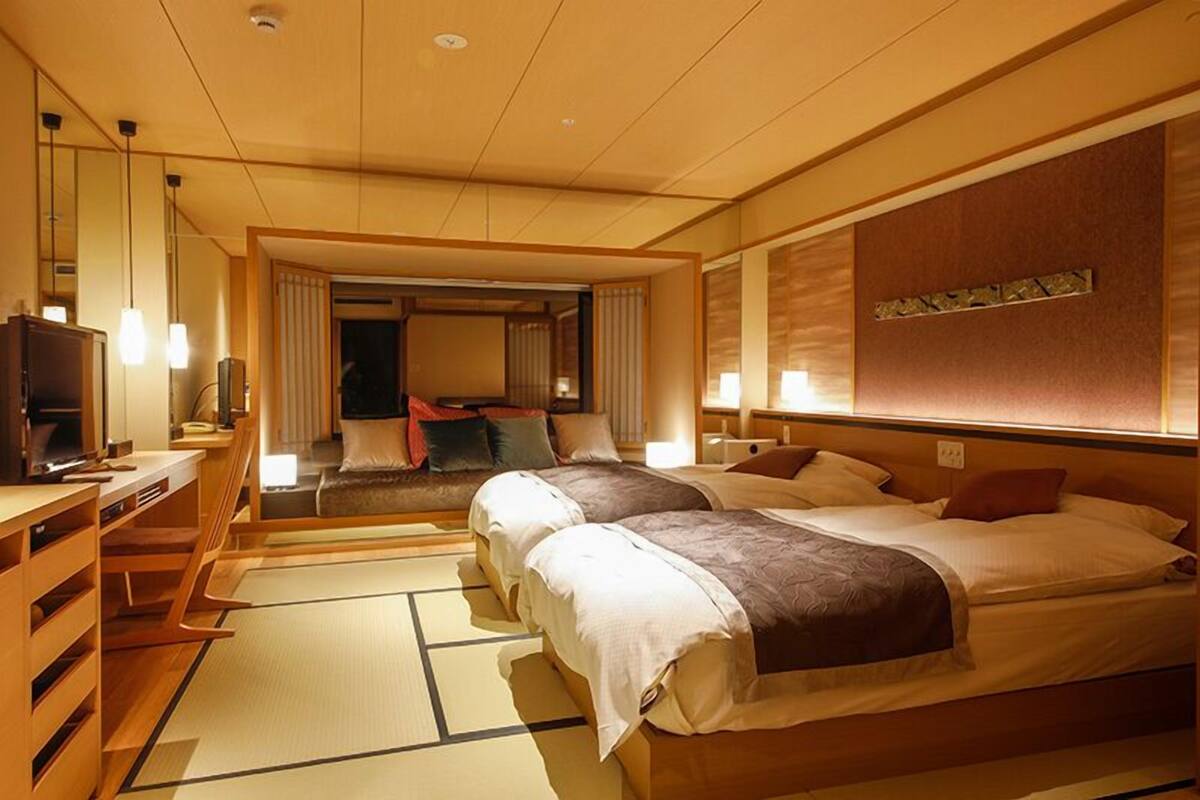 Habitación de hotel con dos camas, un escritorio, un televisor y suelo con esterilla de tatami tradicional.