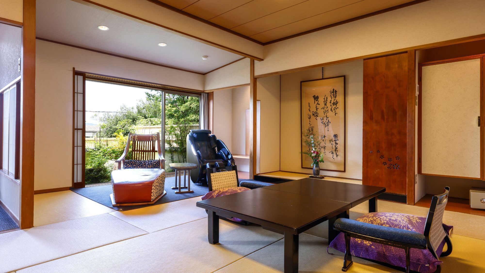 Ein traditioneller japanischer Raum mit Tatami-Boden, einem niedrigen Tisch, einem Massagesessel und einer Schiebetür, die zu einem Garten führt.