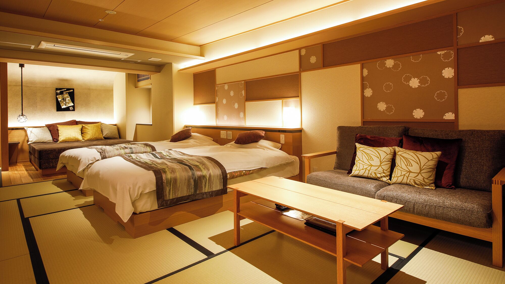 Ein traditionell japanisch gestaltetes Hotelzimmer mit Tatami-Böden, einer Couch, zwei Betten und einem Tisch.