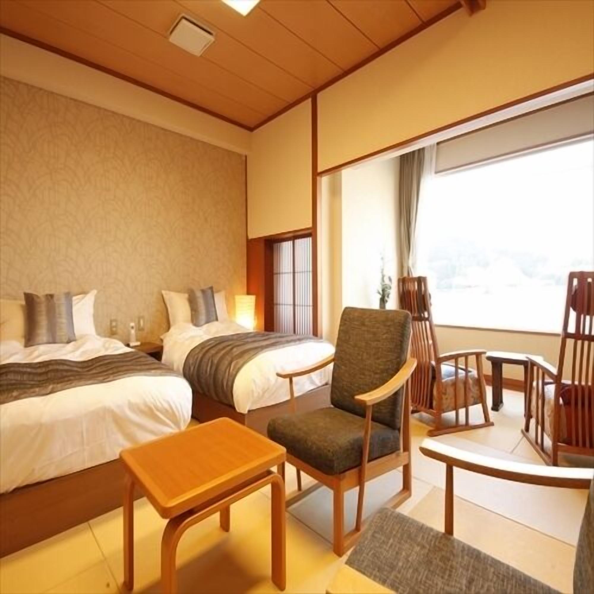 Ein Hotelzimmer mit zwei Betten, einem kleinen Tisch, einem Stuhl und Blick ins Freie.