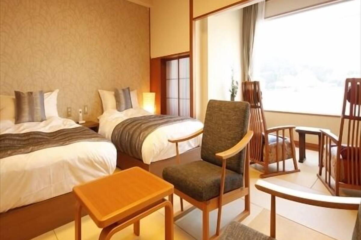 Habitación de hotel con dos camas, una mesita, una silla y vistas al exterior.