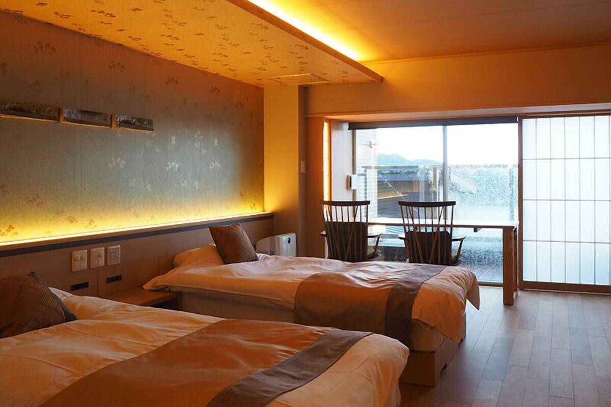 Habitación de hotel con dos camas, una mesa de comedor y vistas amplias por una ventana grande.