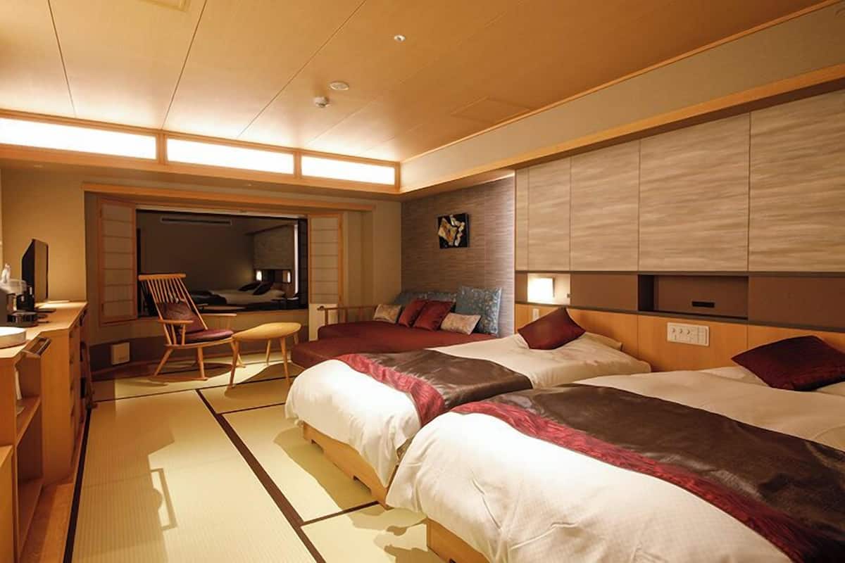 Une chambre d’hôtel avec deux lits, un coin salon comprenant un fauteuil, une petite table et un téléviseur fixé au mur.