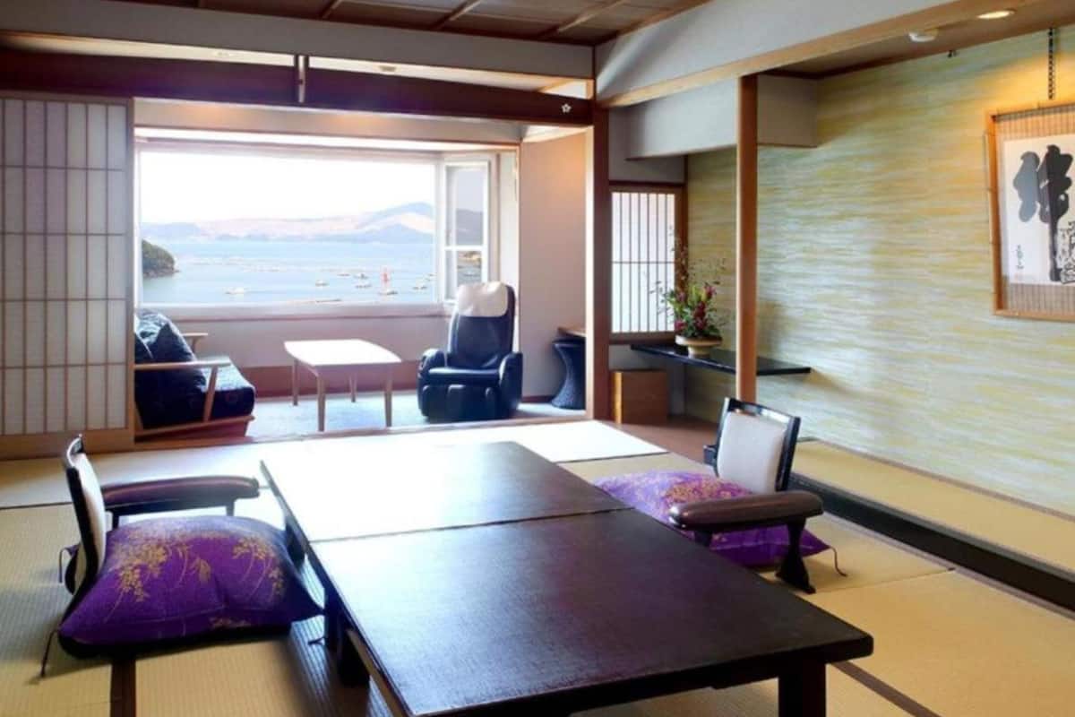 A tatami mat room with a view of the sea, a massage chair, and a traditional Japanese aesthetic.