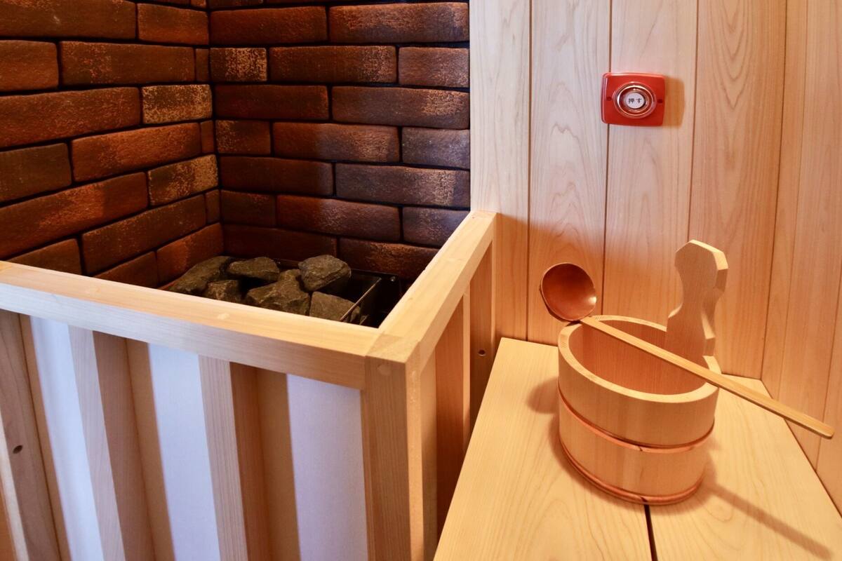 Uma sauna com parede de tijolos, banco de madeira e botão de emergência vermelho.