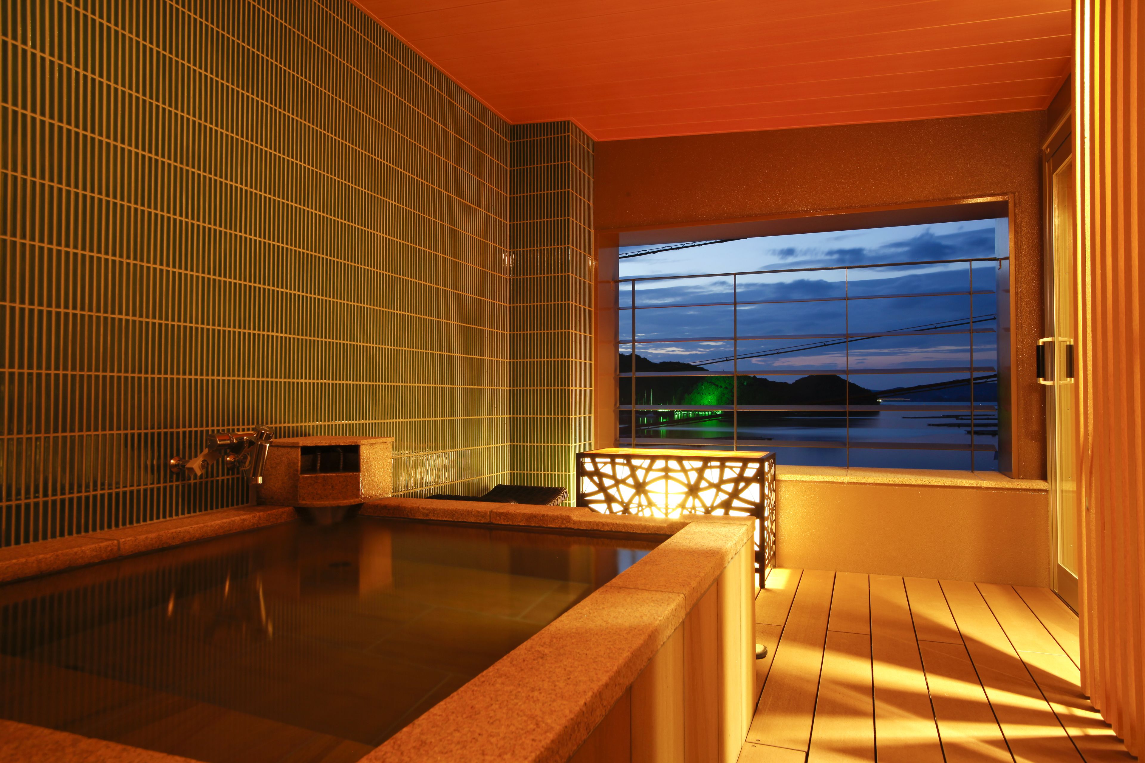 Zona de baños termales con vistas a un cuerpo de agua y colinas al atardecer.
