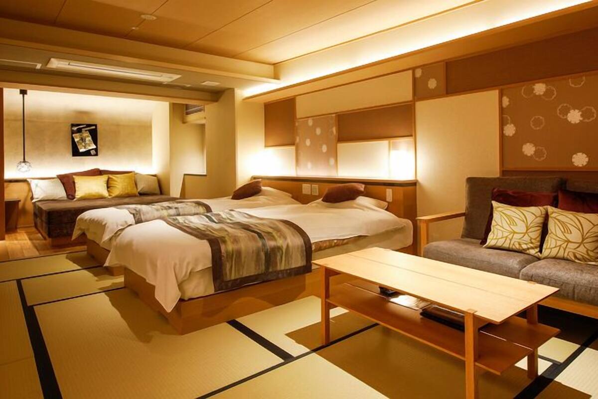 Una habitación de hotel tradicional al estilo japonés, con suelo de tatami, un sofá, dos camas y una mesita.