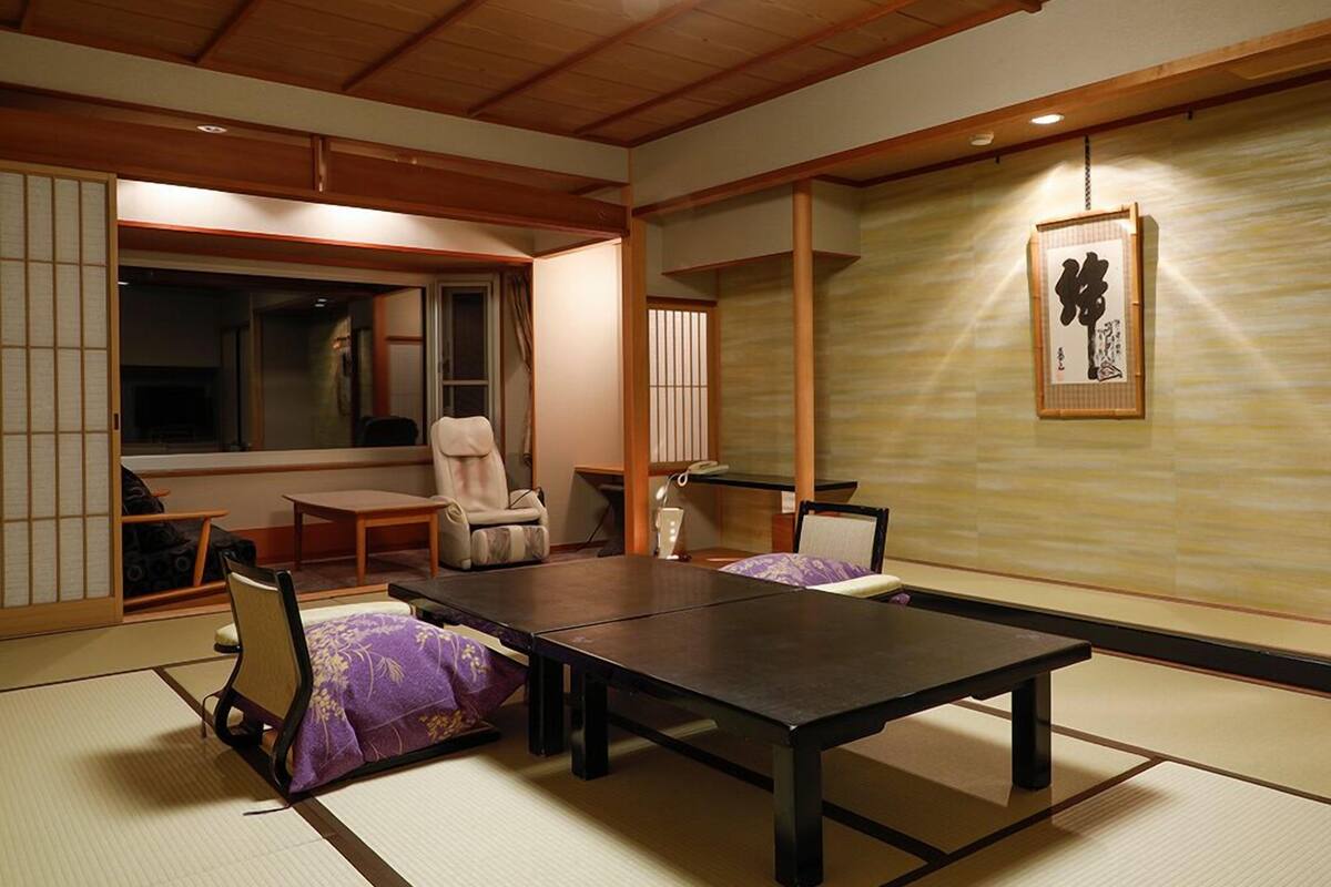 Una habitación japonesa tradicional con suelo de tatami, una mesa baja, sillas y un puertas correderas.