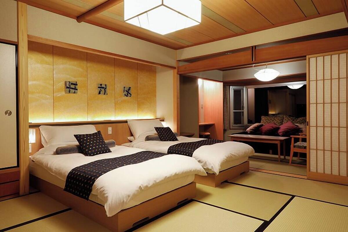 Habitación de hotel de estilo japonés tradicional, con suelo de tatami, dos camas, una puerta corredera y vistas al exterior.