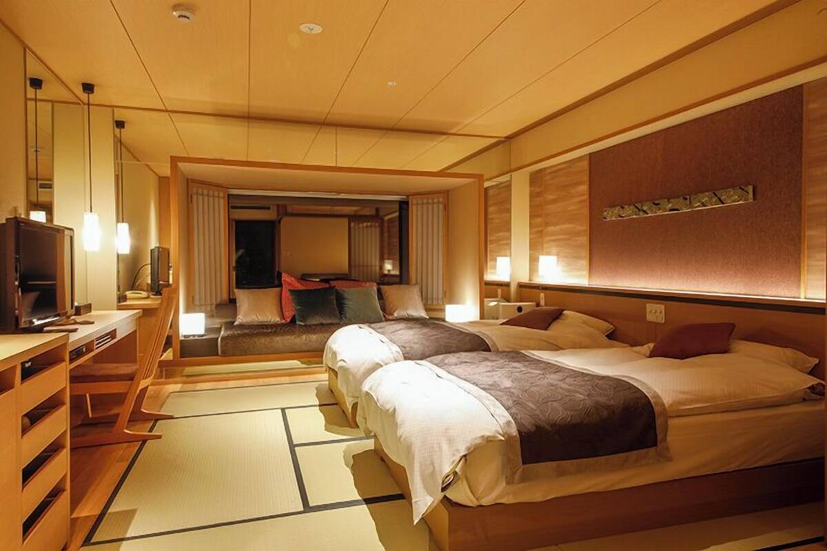 Habitación de hotel con dos camas, televisión, escritorio y suelo con tatami japonés tradicional.