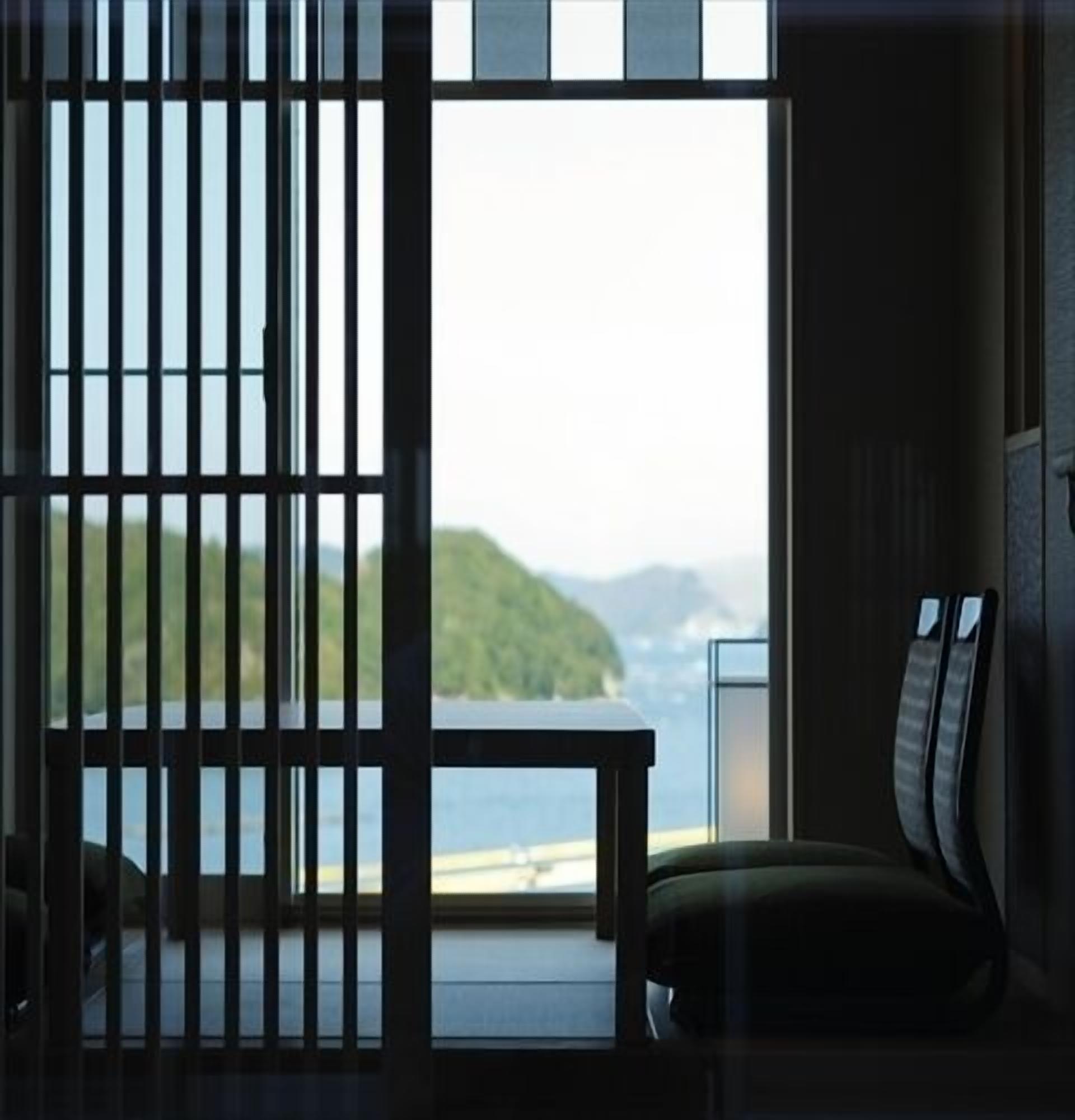 Ein Zimmer mit Blick auf ein Gewässer und ein entferntes Land, eine Schiebetür sowie ein Sessel.