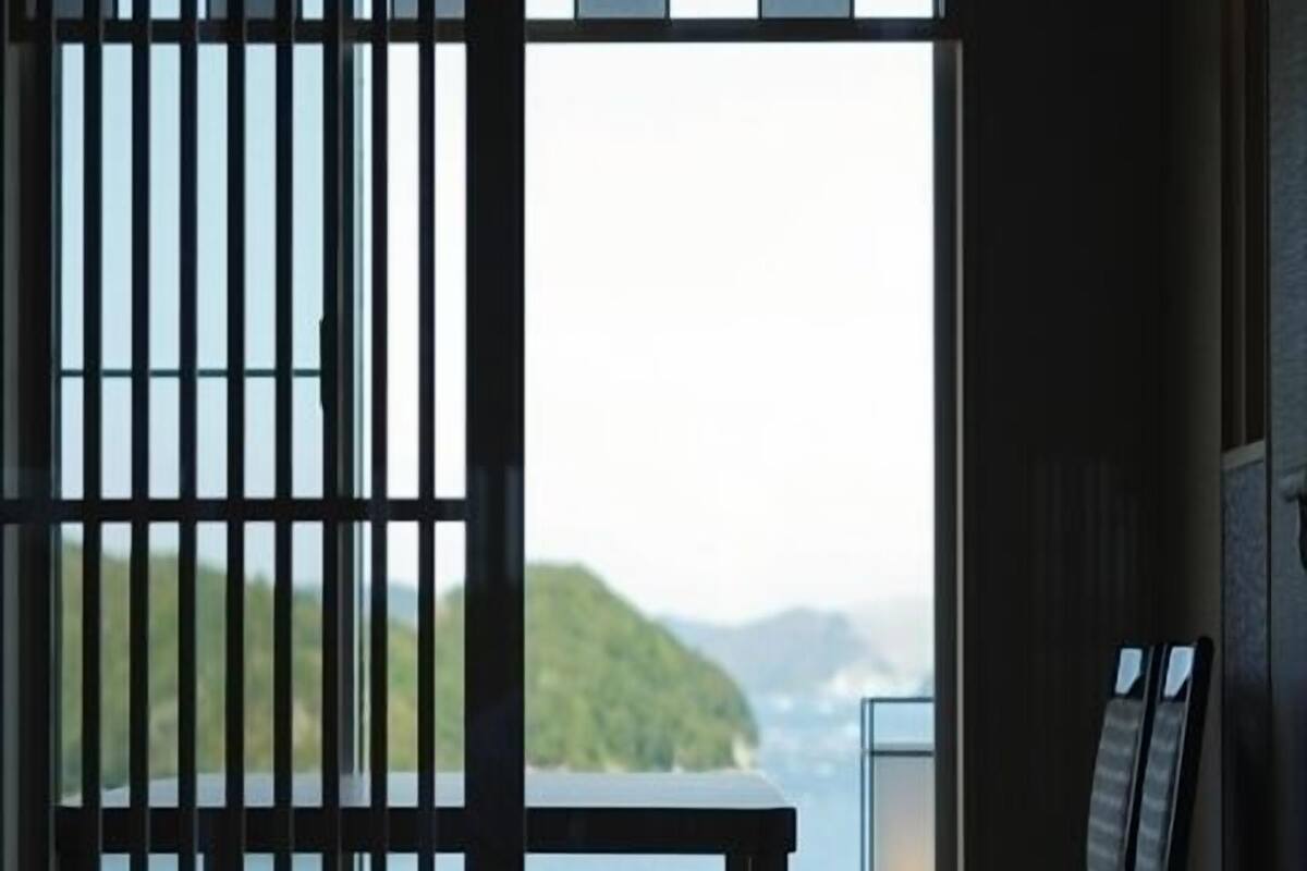 Quarto com vista para um corpo d'água e uma terra distante, porta de correr e uma cadeira.