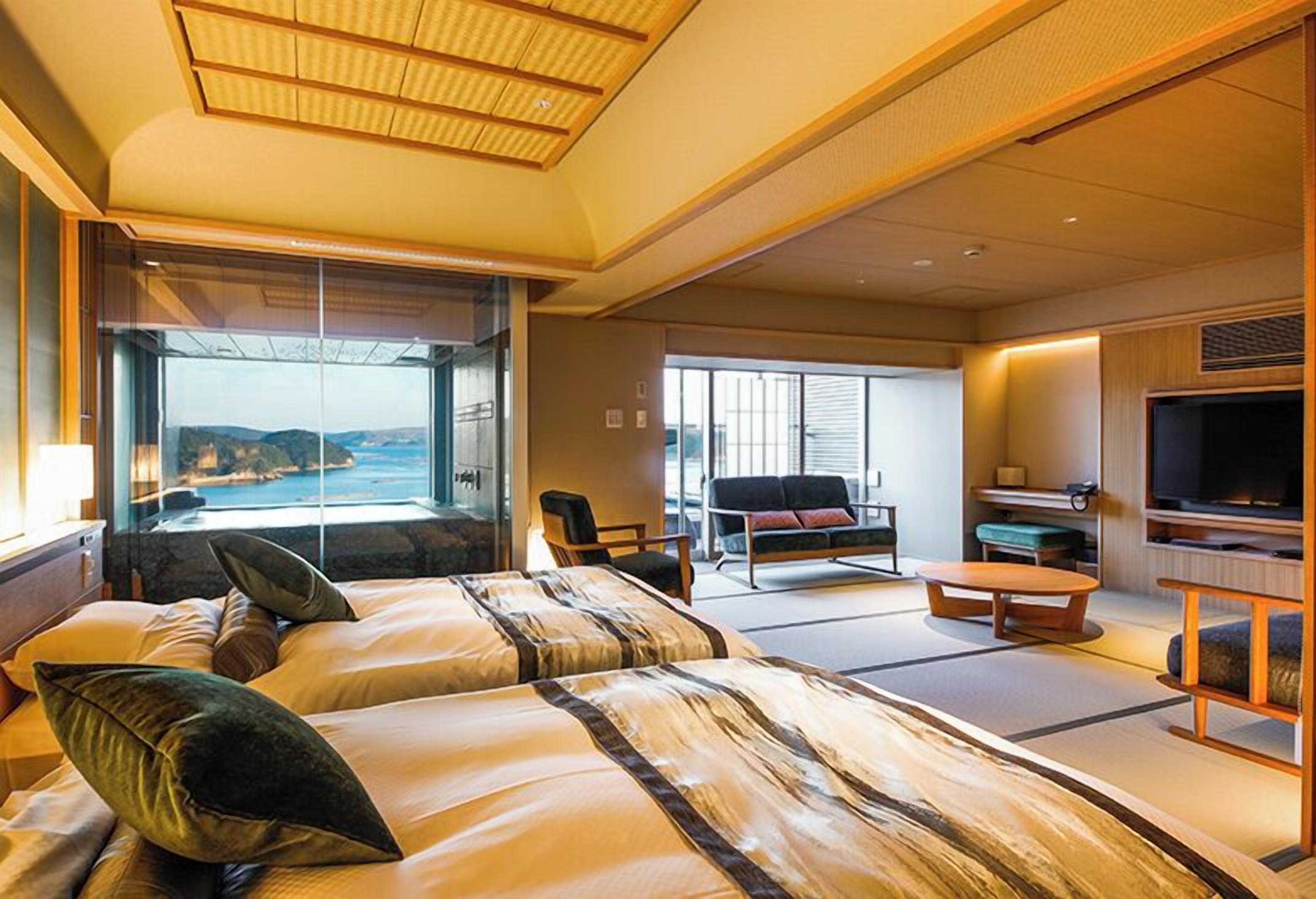 Ein Hotelzimmer mit zwei Betten, einem Fernseher, einer Couch und Meerblick.