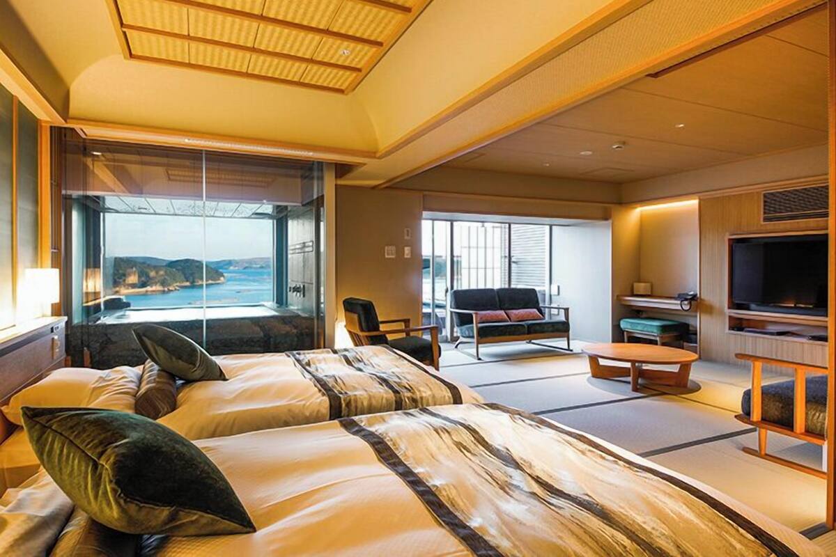 Habitación de hotel con dos camas, televisión, sofá y vista al mar.