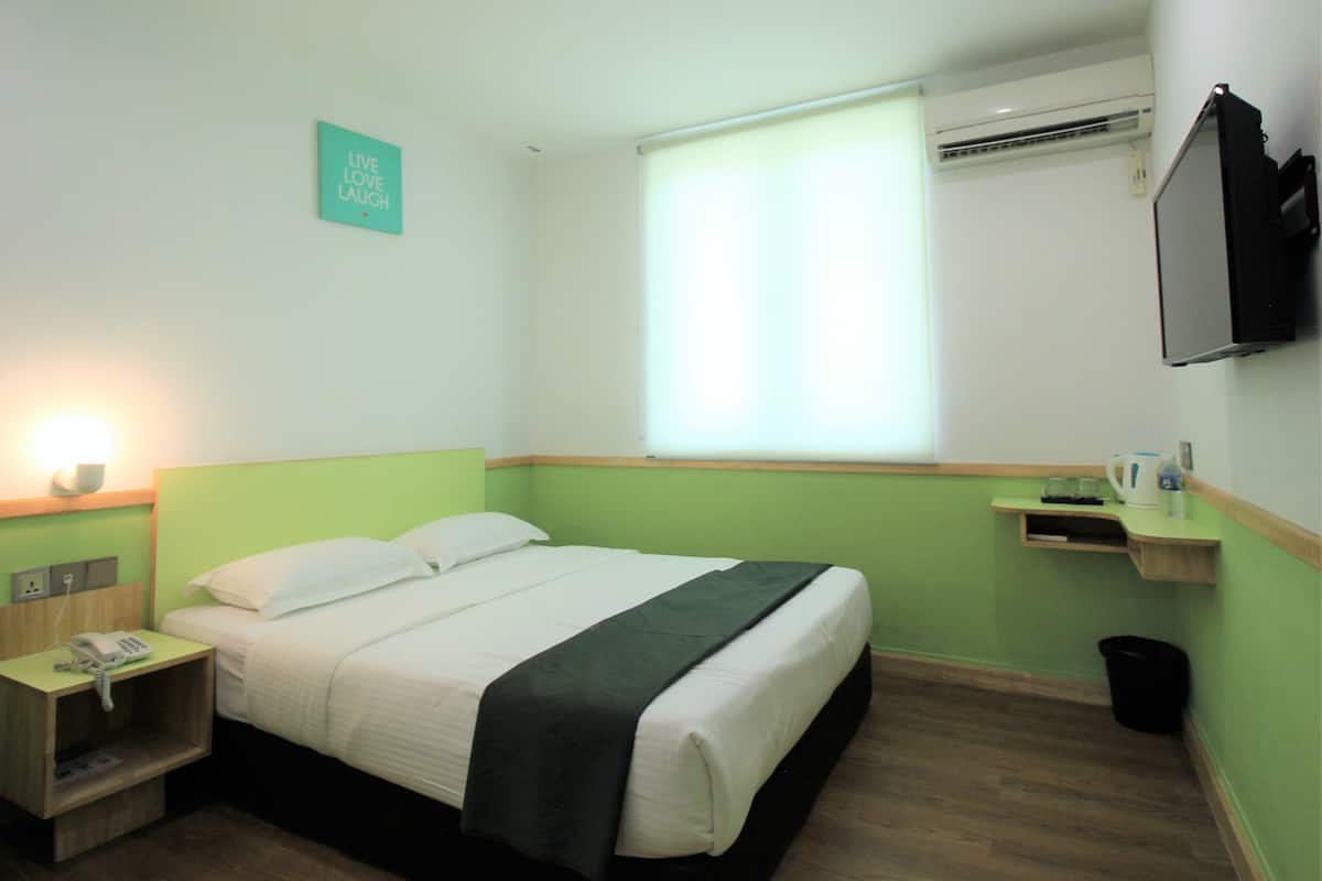 A hotel room with a bed, bedside table, lamp, air conditioning unit, and a television.