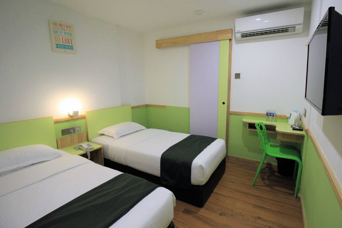 A hotel room with two beds, a desk, a chair, a phone, and a wall-mounted TV.