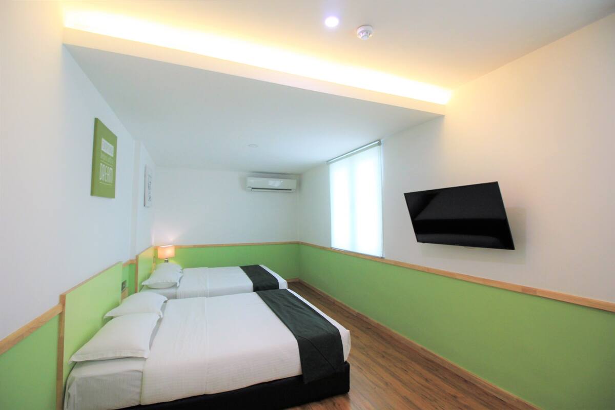 A hotel room with two beds, a flat-screen TV mounted on the wall, and a window providing natural light.