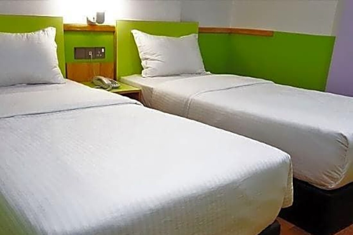 A room with two single beds, each with a green headboard and white bedding. There is a nightstand with a telephone and a lamp between the beds.