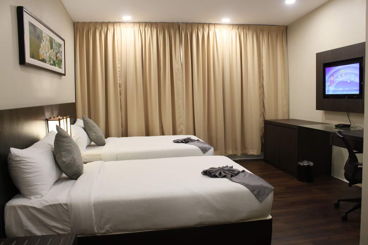 A hotel room with two beds, a desk, a television, and a framed picture on the wall.