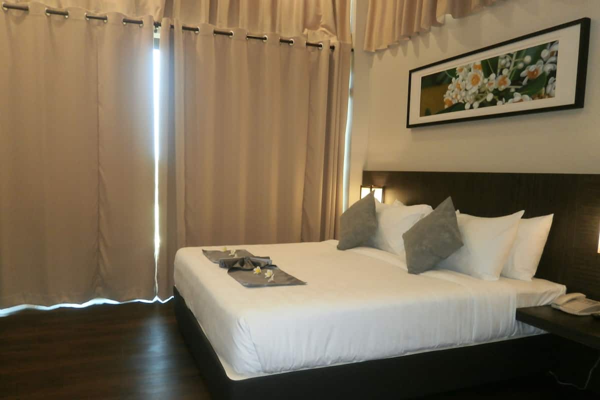 A neatly made bed with pillows and a folded towel, a bedside table with a phone, and a framed picture on the wall.