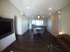 A modern living room with a flat-screen TV, a dining area with a round table and chairs, a sofa, and a patterned rug.