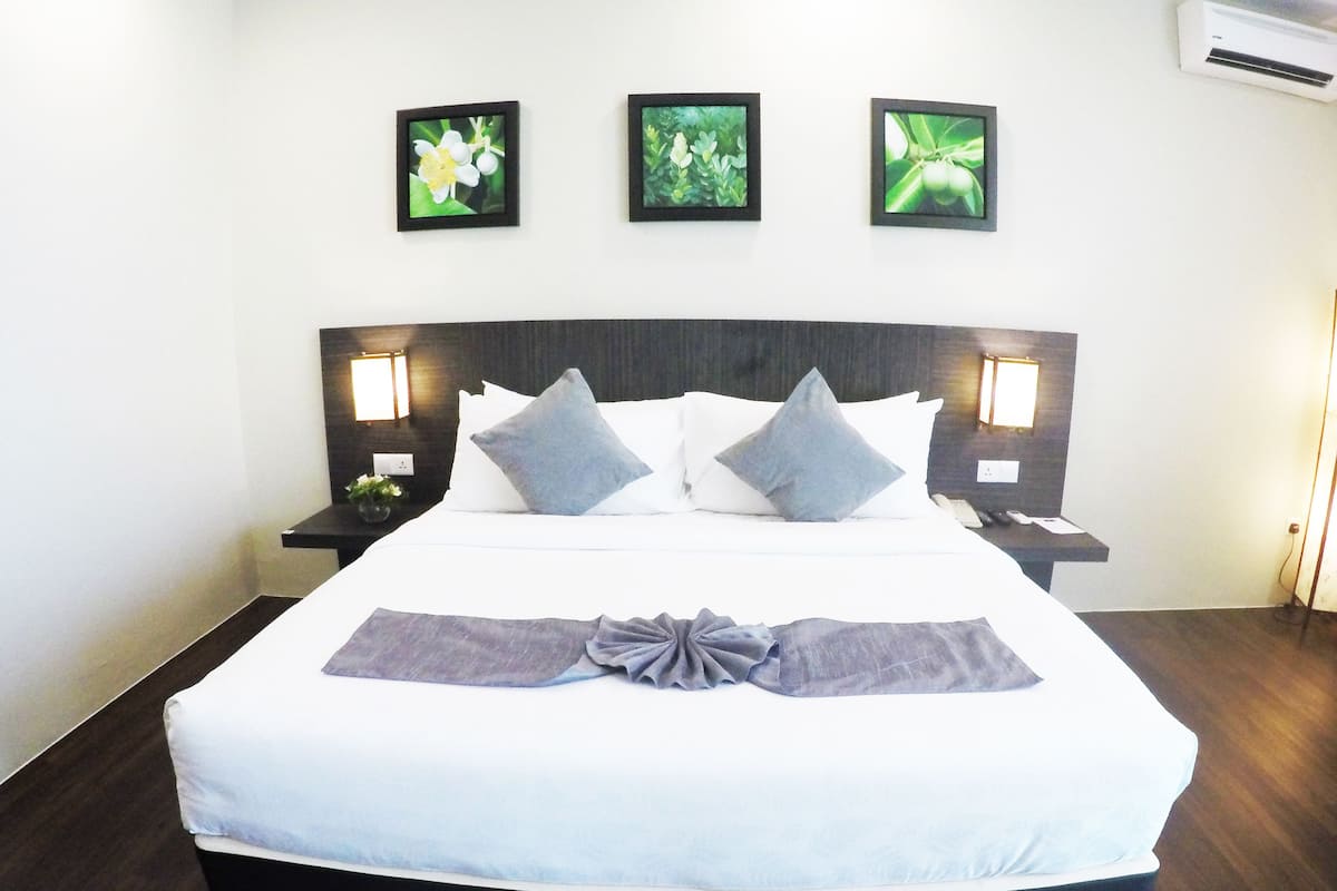 A hotel room with a large bed, two bedside tables, a wall-mounted air conditioner, and three framed pictures above the bed.