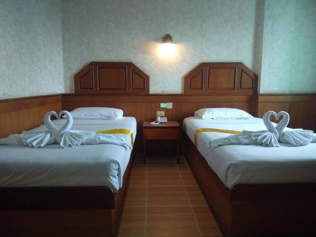 Habitación de hotel con dos camas, una mesita de noche y una lámpara fijada en la pared.