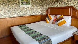 Un lit bien fait, avec une couvre-lit à motifs et plusieurs oreillers, une tête de lit en bois et un papier peint à motifs floraux.