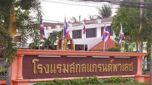 Un bâtiment orné d’une enseigne en écriture thaïlandaise, entouré de drapeaux et de palmiers.