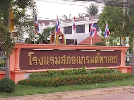 A building with a sign in Thai script, surrounded by flags and palm trees.