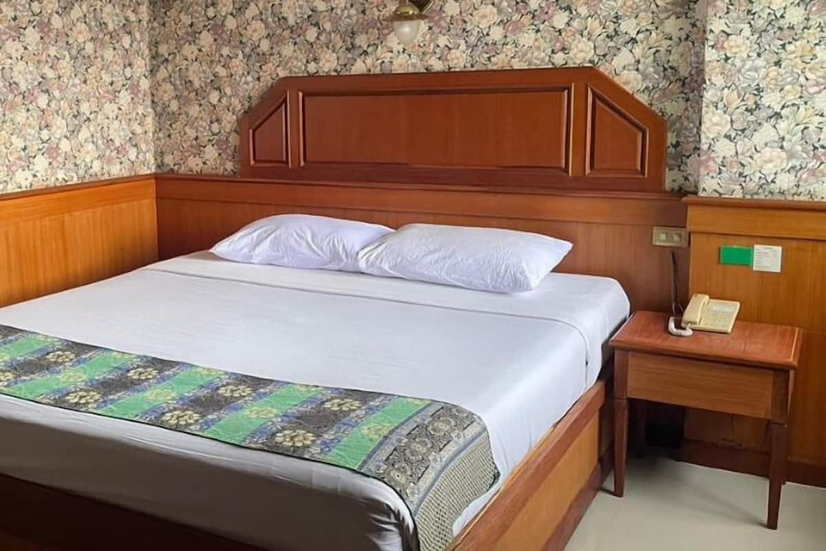 Ein Hotelzimmer mit einem hölzernen Kopfteil, einem Bett mit weißer Bettwäsche, einer gemusterten Tagesdecke und einem Nachttisch mit Telefon.