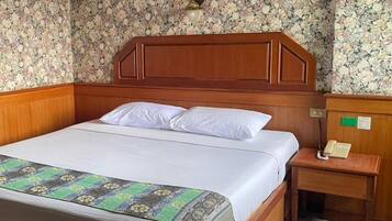 Habitación de hotel con cabecera de madera, cama con ropa blanca, manta con estampado y mesita de noche con teléfono.