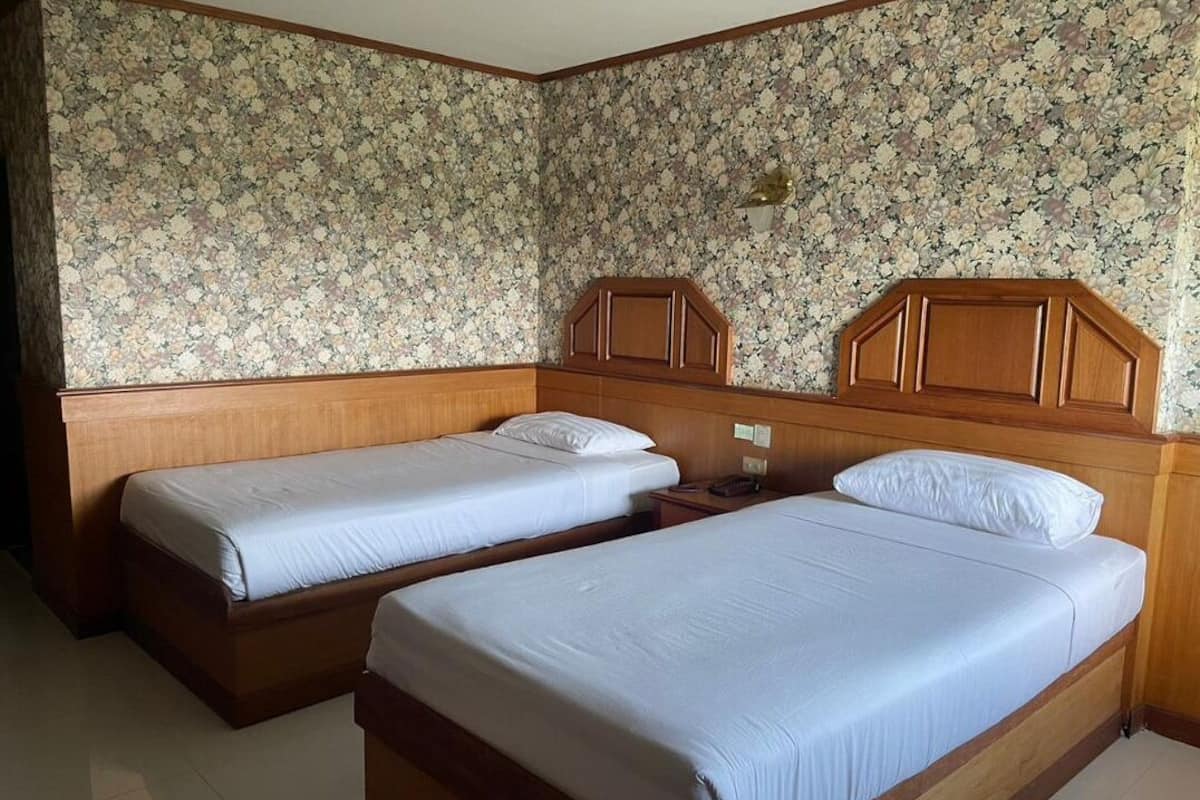 Ein Zimmer mit zwei Einzelbetten, Holz-Kopfteilen und floralem Wandpapier.