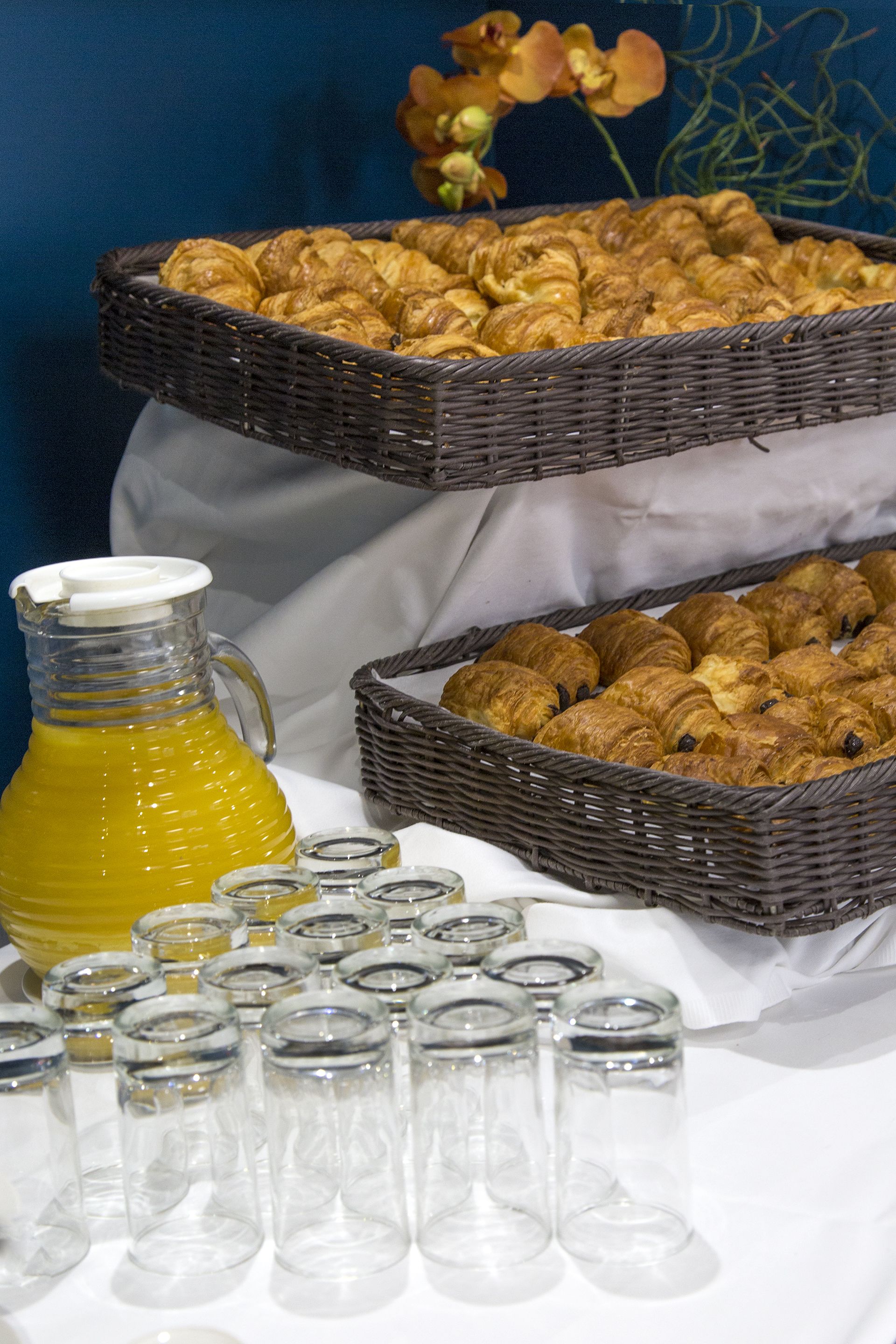A table with baskets of pastries and a pitcher of juice.