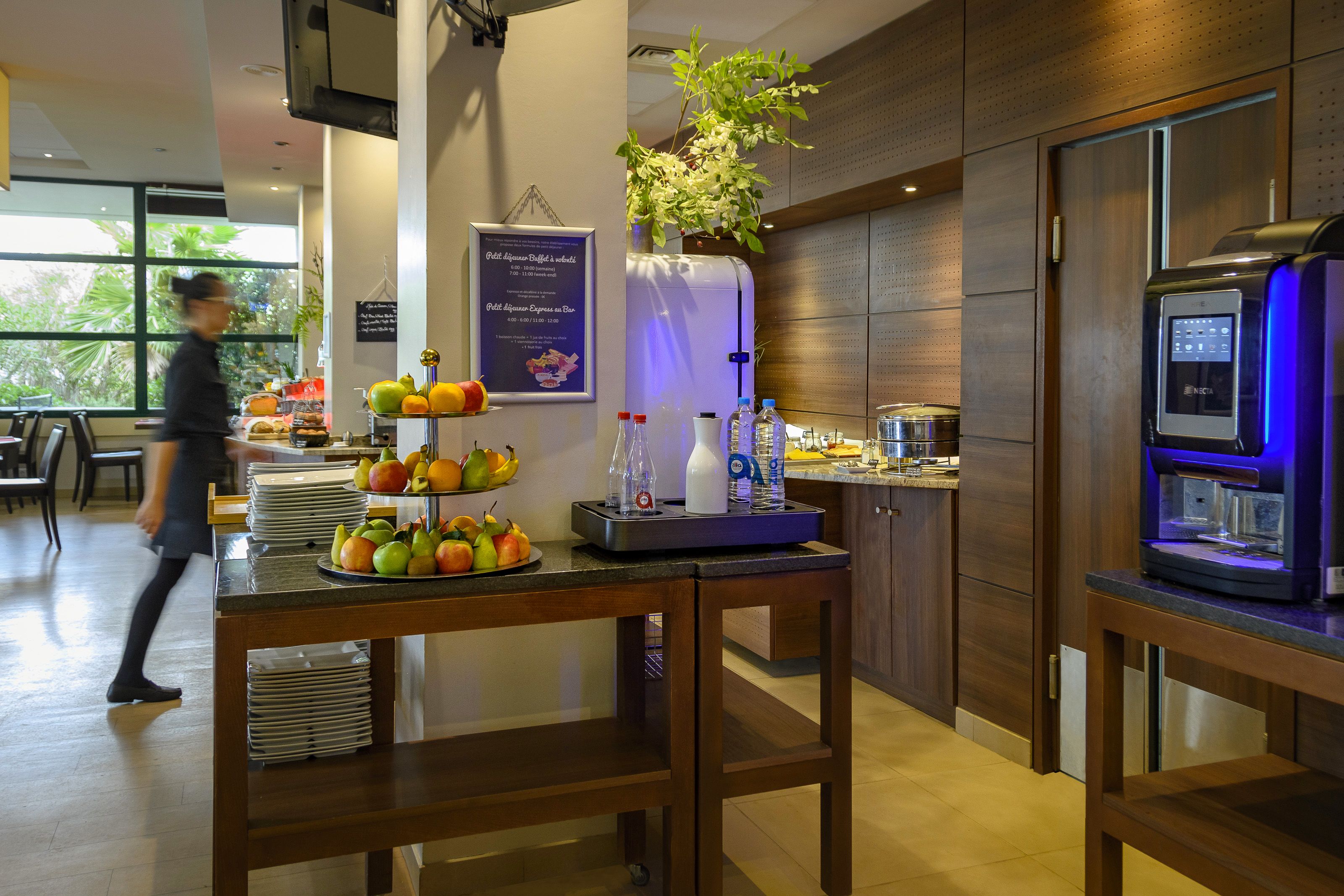 Una barra de desayuno con fruta, una máquina de café y un dispensador de agua.