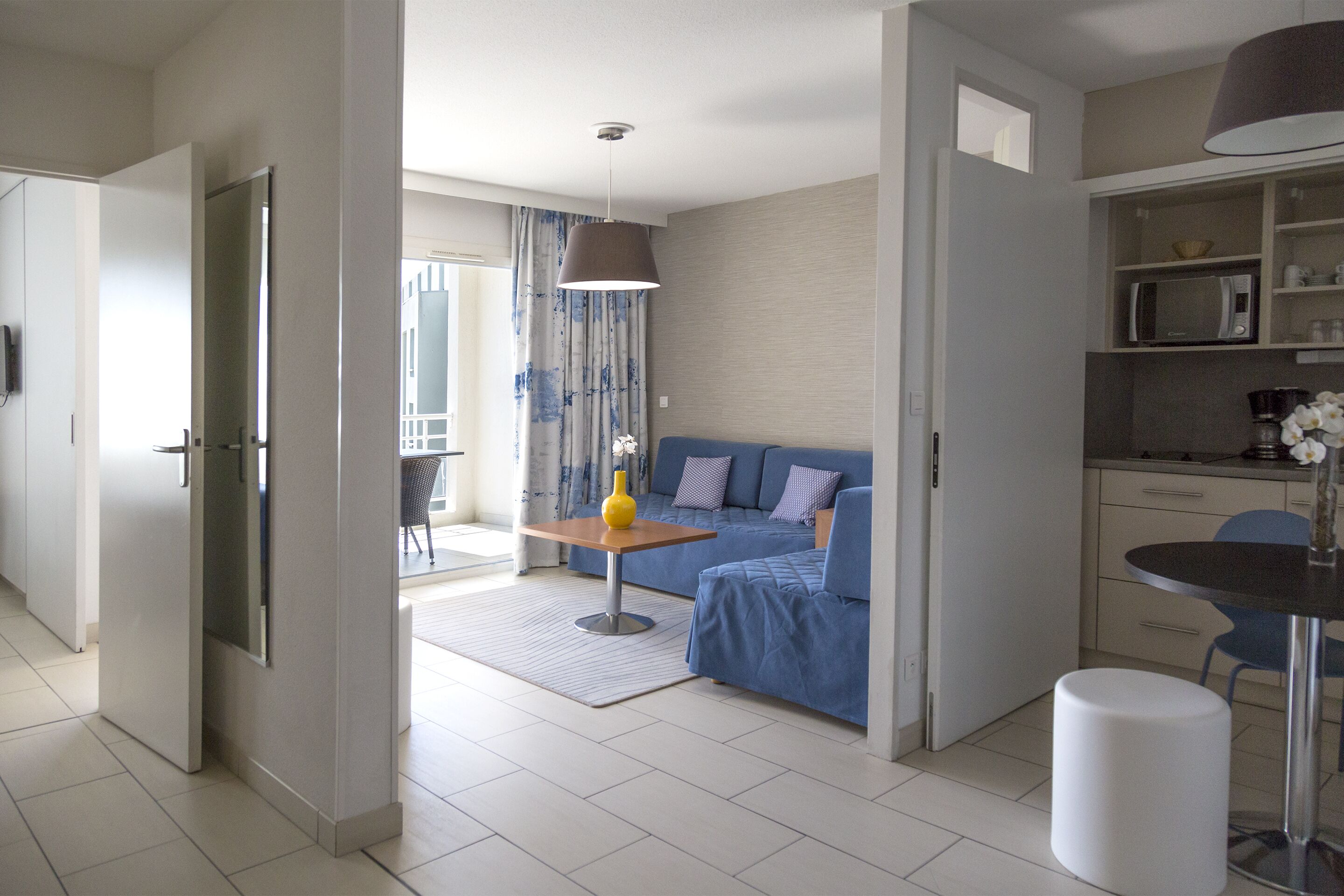 Uma sala de estar moderna com um sofá azul, uma mesa de madeira pequena e um banquinho cilíndrico branco.