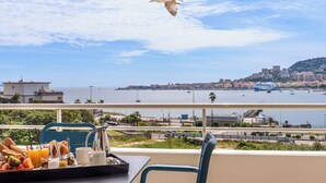 A balcony with a breakfast tray, a chair, and a view of the sea and cityscape. - Résidence de Tourisme Ajaccio Amirauté (Ajaccio)