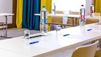 A conference room with white tables, water bottles, glasses, and blue pens.