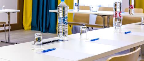 A conference room with white tables, water bottles, glasses, and blue pens.