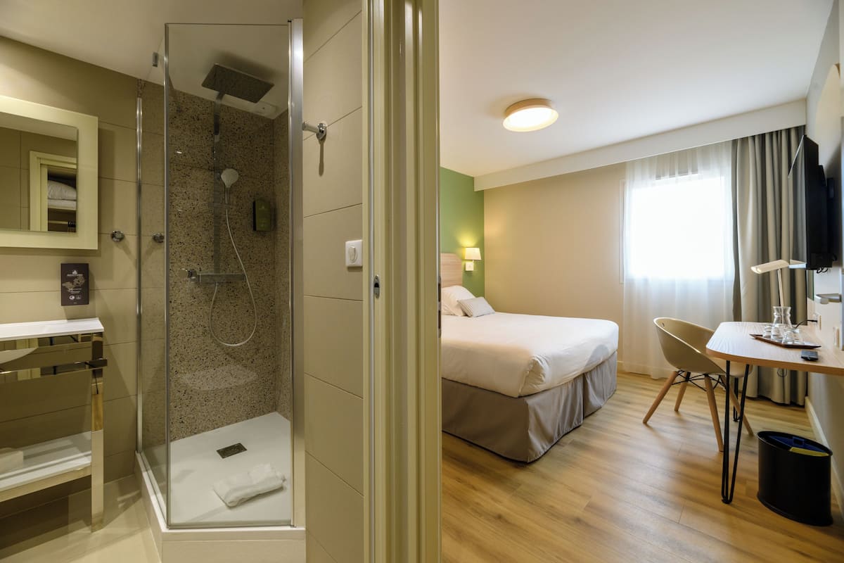 Ein Hotelzimmer mit einer Duschkabine, einem Bett, einem Schreibtisch mit Stuhl und einem Fernseher.
